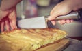 Cooking at home concept: vintage faded image of a womanÃ¢â¬â¢s hands cutting a potato pie with chefÃ¢â¬â¢s knife in the kitchen